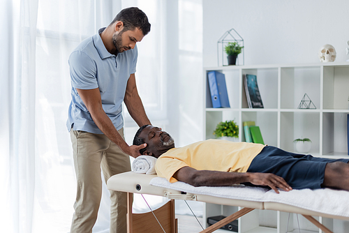 african american man with closed eyes lying on massage table during rehabilitation treatment