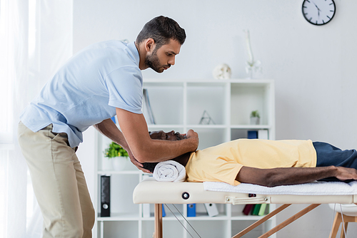side view of young physiotherapist treating african american patient in rehab center