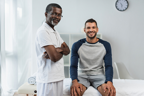 happy african american doctor and cheerful patient looking at camera in rehabilitation center