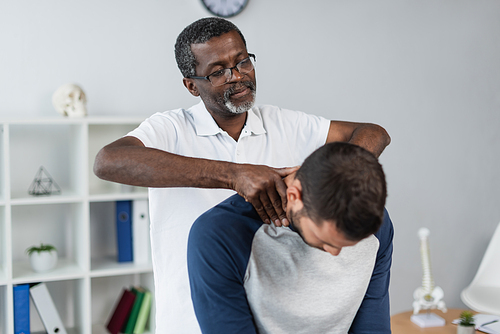 mature african american physiotherapist examining neck of young man in rehabilitation center