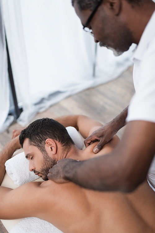 young man getting back and shoulder massage from african american masseur