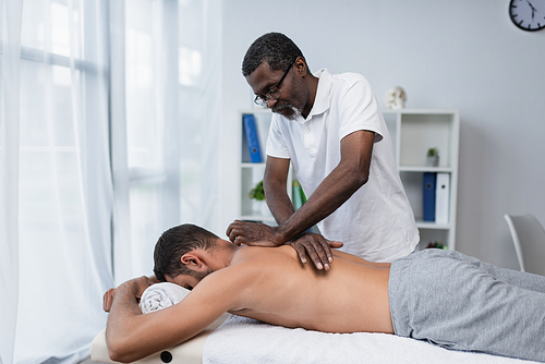 mature african american rehabilitologist doing back massage to young man