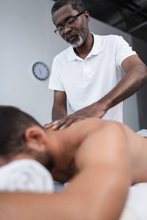 low angle view of african american masseur doing back massage during rehabilitation of blurred man