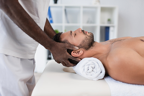 side view of young man getting treating massage by african american rehabilitologist