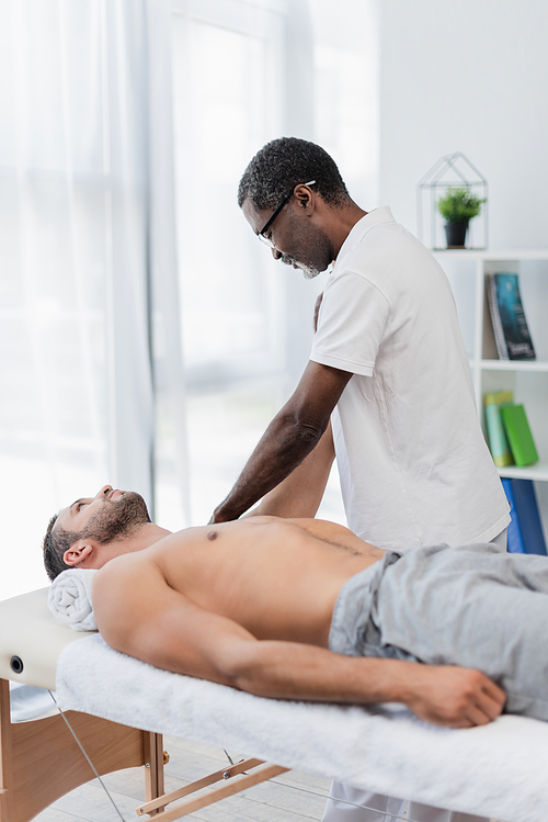 african american physical therapist massaging man in rehab center