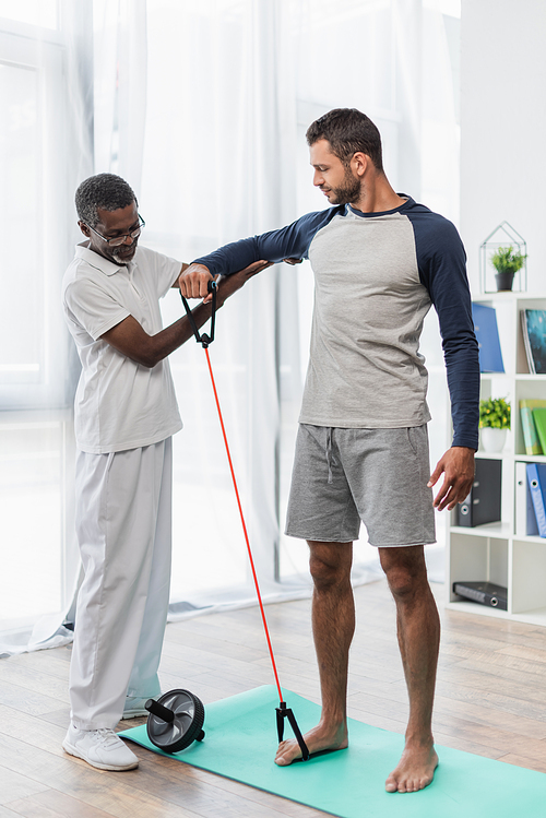 mature african american physical therapist assisting barefoot man working out with resistance band
