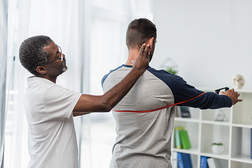 african american rehabilitation trainer assisting man working out with resistance band