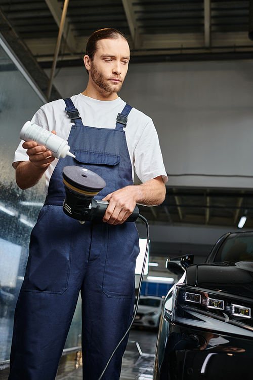 handsome hard working serviceman in uniform applying paste on polishing machine while in garage