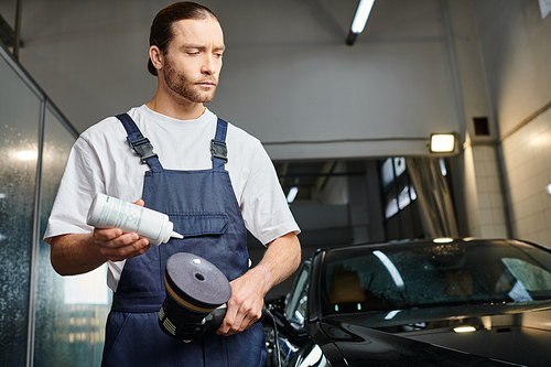 good looking dedicated professional in comfy uniform applying paste on polishing machine in garage