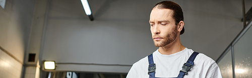 good looking professional serviceman in blue comfy uniform posing in garage and looking away