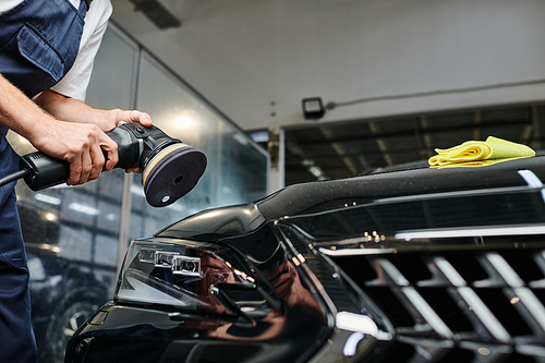 cropped view of professional hard working specialist using polishing machine on black modern car