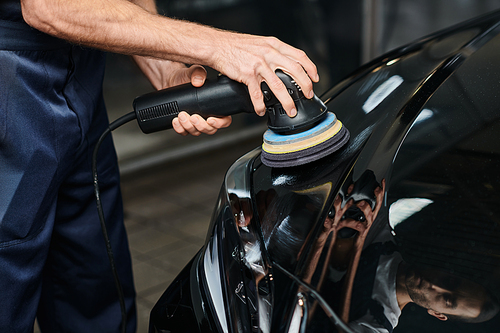 cropped view of hard working dedicated serviceman using polishing machine on black modern car