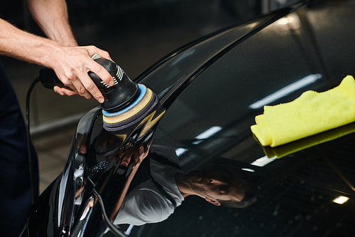 cropped view of hard working professional specialist working with polishing machine on black car