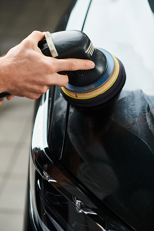 cropped view of hard working serviceman using carefully polishing machine on black modern car