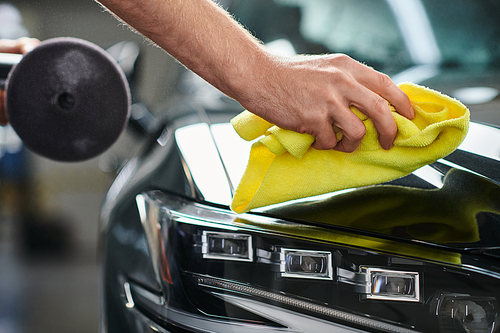 cropped view of hard working professional serviceman with polishing machine cleaning car with rag