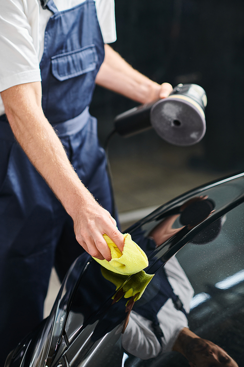 cropped view of dedicated specialist cleaning modern black car with rag holding polishing machine