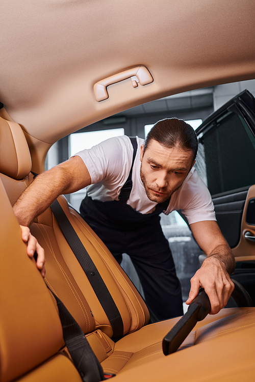 good looking dedicated serviceman in uniform with collected hair using manual vacuum cleaner in car