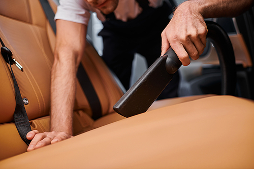 cropped view of hard working professional serviceman working with manual vacuum cleaner in car