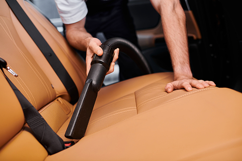 cropped view of devoted hard working specialist using manual vacuum cleaner in car in garage