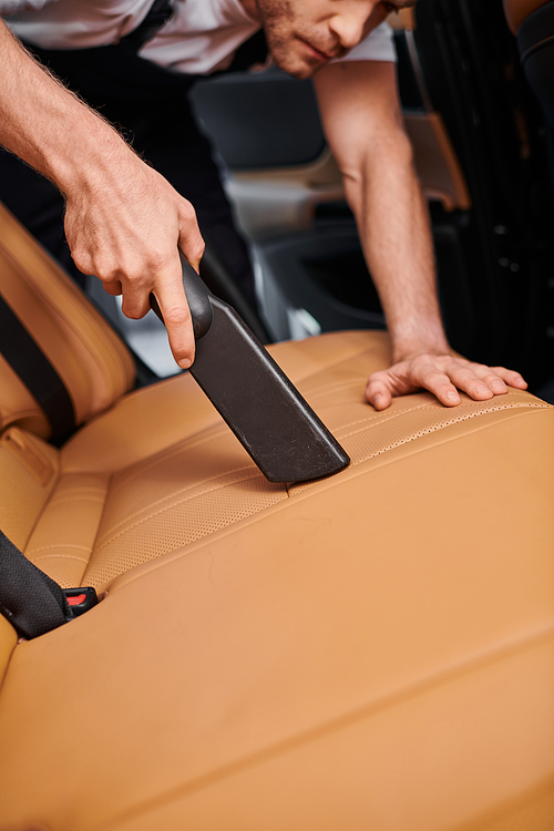 cropped view of dedicated professional worker using manual vacuum cleaner on car while in garage