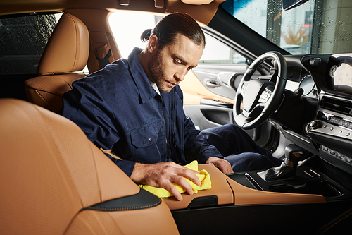 appealing devoted serviceman in blue uniform with collected hair cleaning car with yellow rag