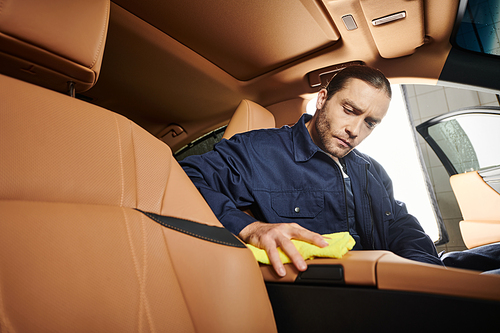 handsome dedicated professional serviceman in uniform with collected hair cleaning car with rag