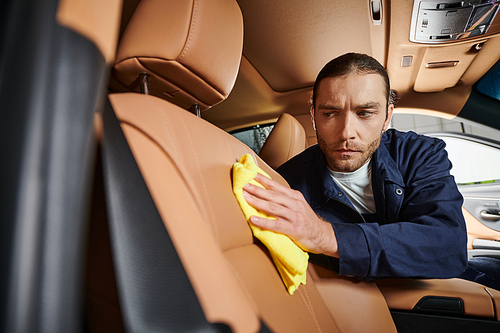 attractive hard working professional serviceman in uniform with collected hair cleaning car with rag