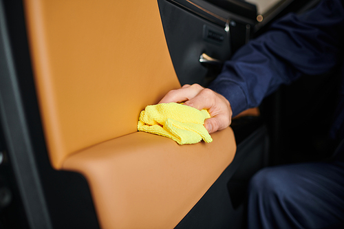 cropped view of hard working dedicated specialist in blue uniform cleaning car with yellow rag