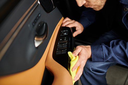 cropped view of hard working specialist in blue uniform cleaning attentively car with yellow rag