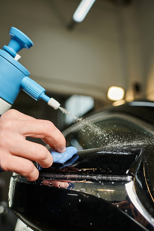 cropped view of hard working man in uniform cleaning side view mirror using pulverizer and rag