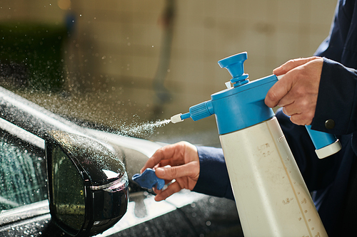 cropped view of devoted professional in uniform using pulverizer and rag to clean side view mirror