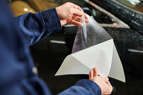 cropped view of hard working man in blue uniform ready to apply protective foil on black car