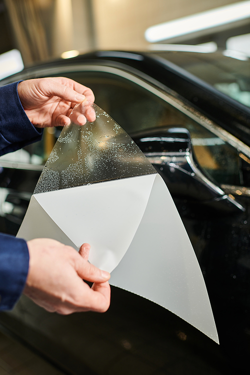 cropped view of hard working specialist in blue uniform ready to apply protective foil on car mirror