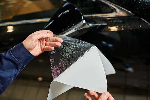 cropped view of devoted specialist in comfy blue uniform applying protective foil on mirror of car