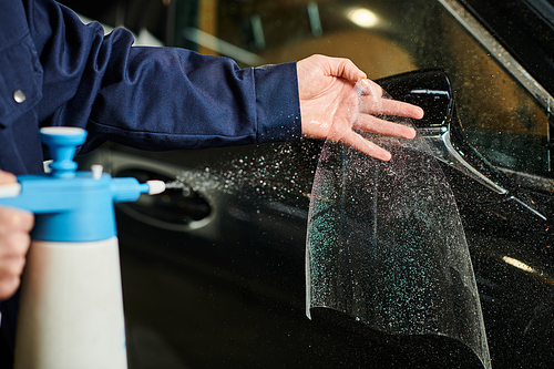 cropped view of devoted professional in blue comfy uniform applying protective foil on mirror of car