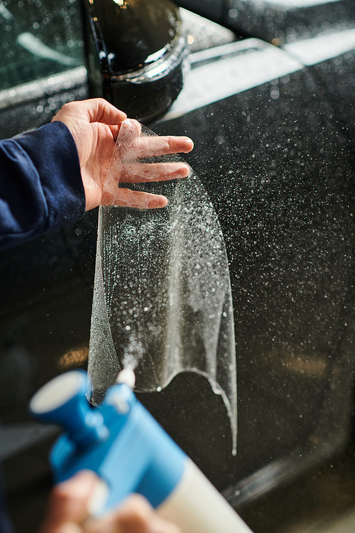 cropped view of hard working serviceman in uniform applying protective foil on side view mirror