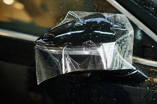 object photo of side view mirror of black new auto with partially applied protective foil on it