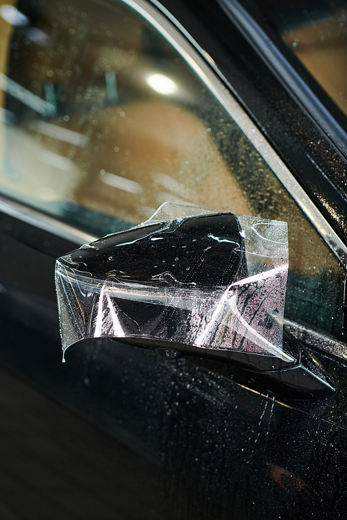 object photo of side view mirror of black modern car with partly applied protective foil on it