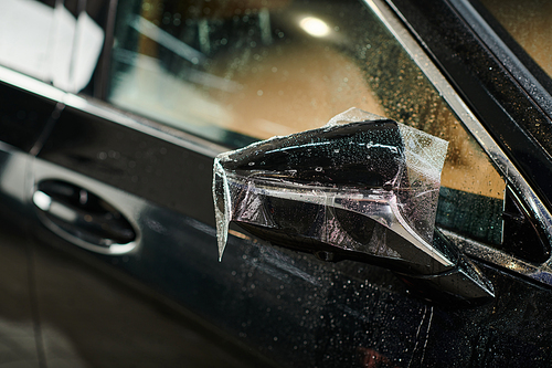 object photo of protective film  applied carefully on side view mirror of black modern car