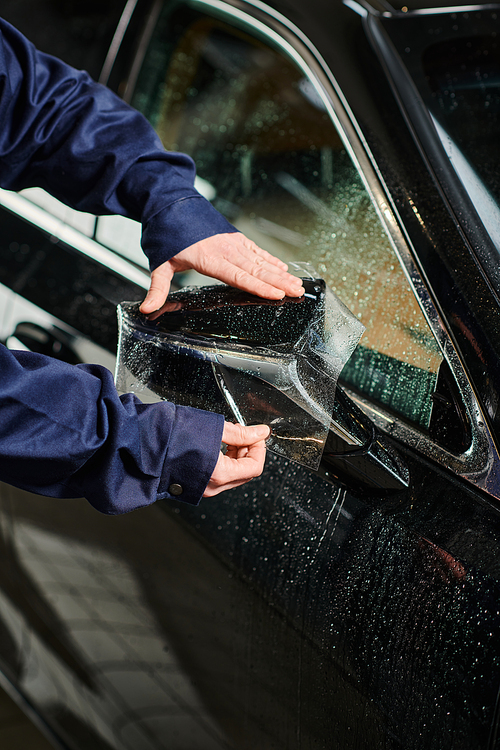 cropped view of hard working professional serviceman in blue uniform applying protective foil on car