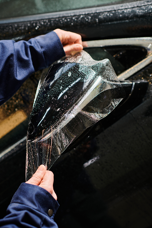 cropped view of professional hard working serviceman in uniform applying protective foil on car