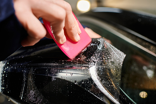 cropped view of professional hard working serviceman applying protective foil carefully on black car