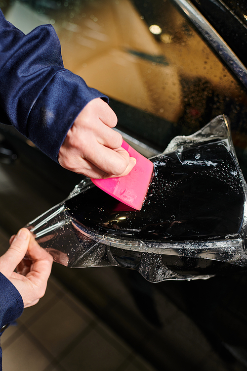 cropped vie of devoted hard working serviceman applying protective foil on side view mirror