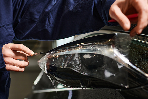 cropped view of hard working serviceman applying protective foil carefully on black car in garage