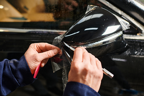 cropped view of dedicated professional male worker applying protective foil on black car mirror