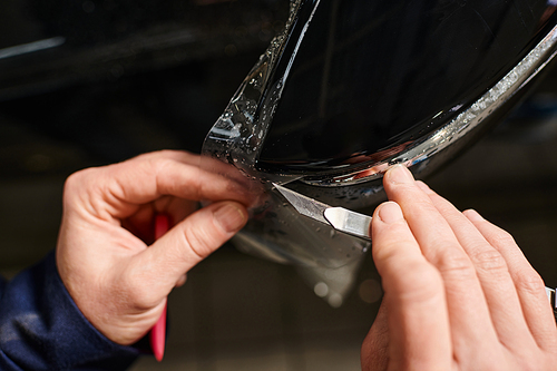 cropped view of hard working professional worker applying protective foil on black car in garage