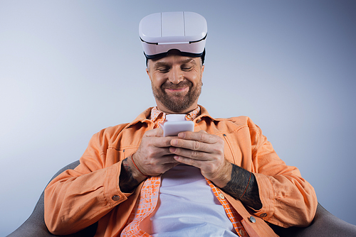 A man in an orange shirt is focused on his cell phone, interacting with the device.