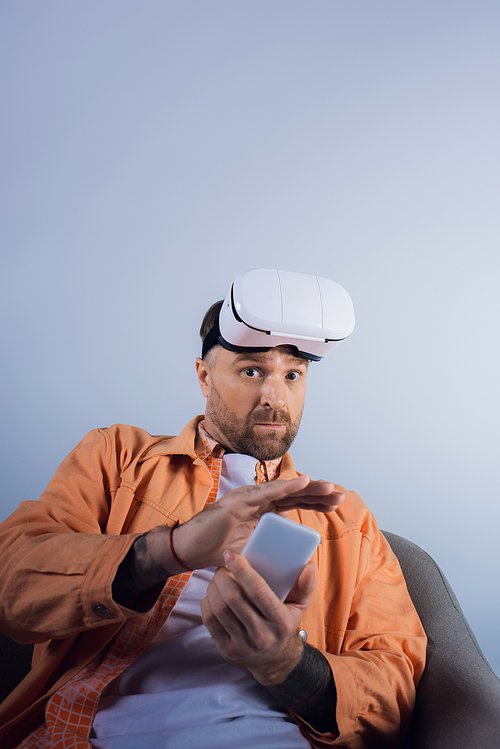 A man immersed in virtual reality, sitting in a chair, engrossed in his cell phone.