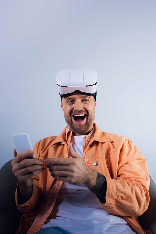 Man sitting in chair, immersed in phone screen, surrounded by virtual reality technology in a studio setting.