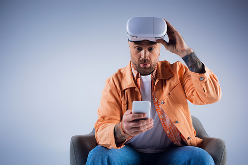 A man in a chair holds a smartphone in a studio setting, immersed in the world of the metaverse through his VR headset.